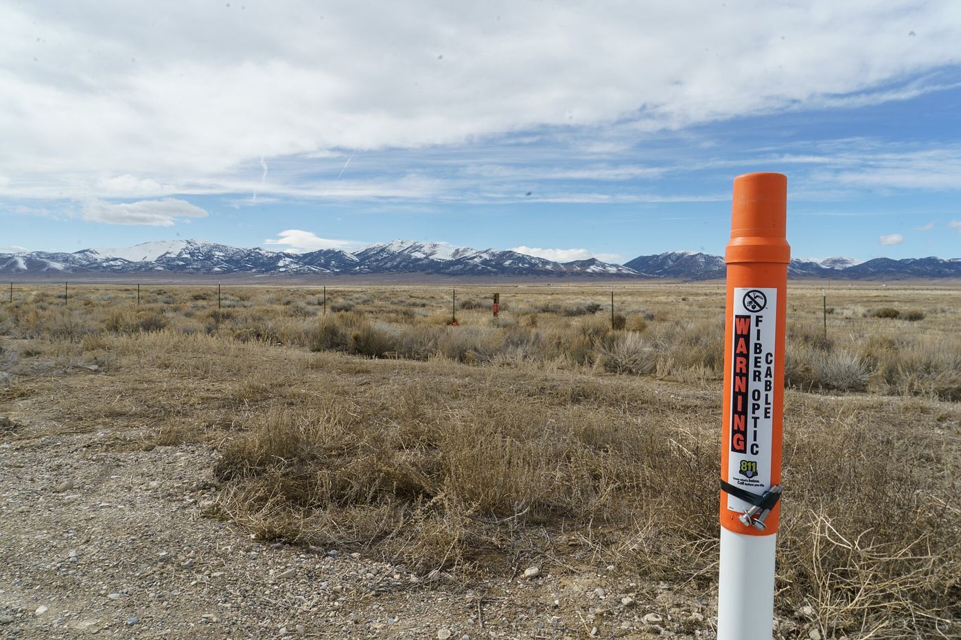 An orange marker post in open country warns of a buried fiber-optic cable